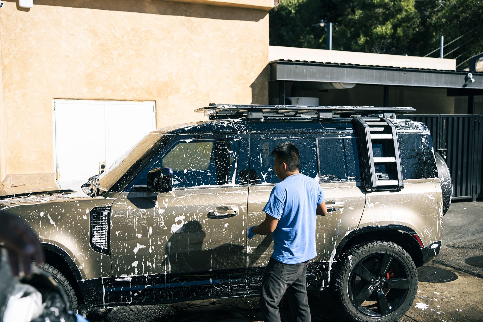 An attendant pressure-rinsing a soapy Land Rover Defender by hand