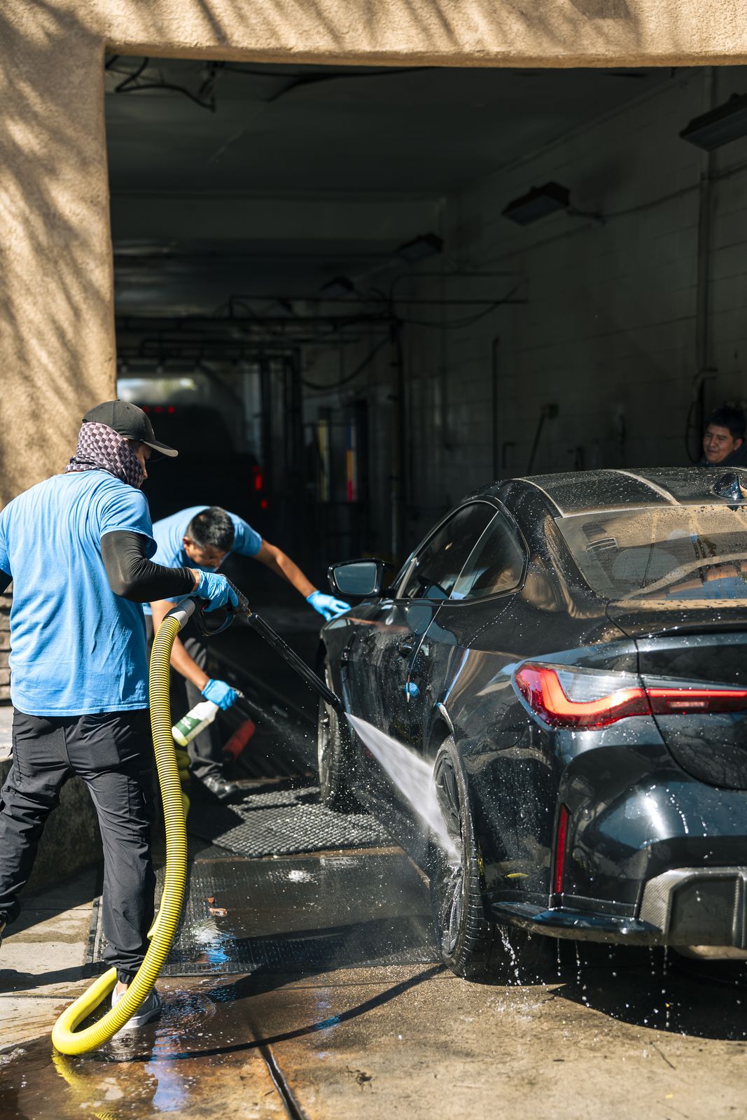 An attendant pressure-washing a black BMW M by hand