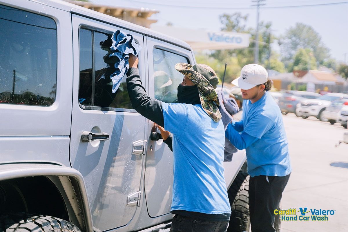 Two crew members washing a white Jeep at the Valero lot